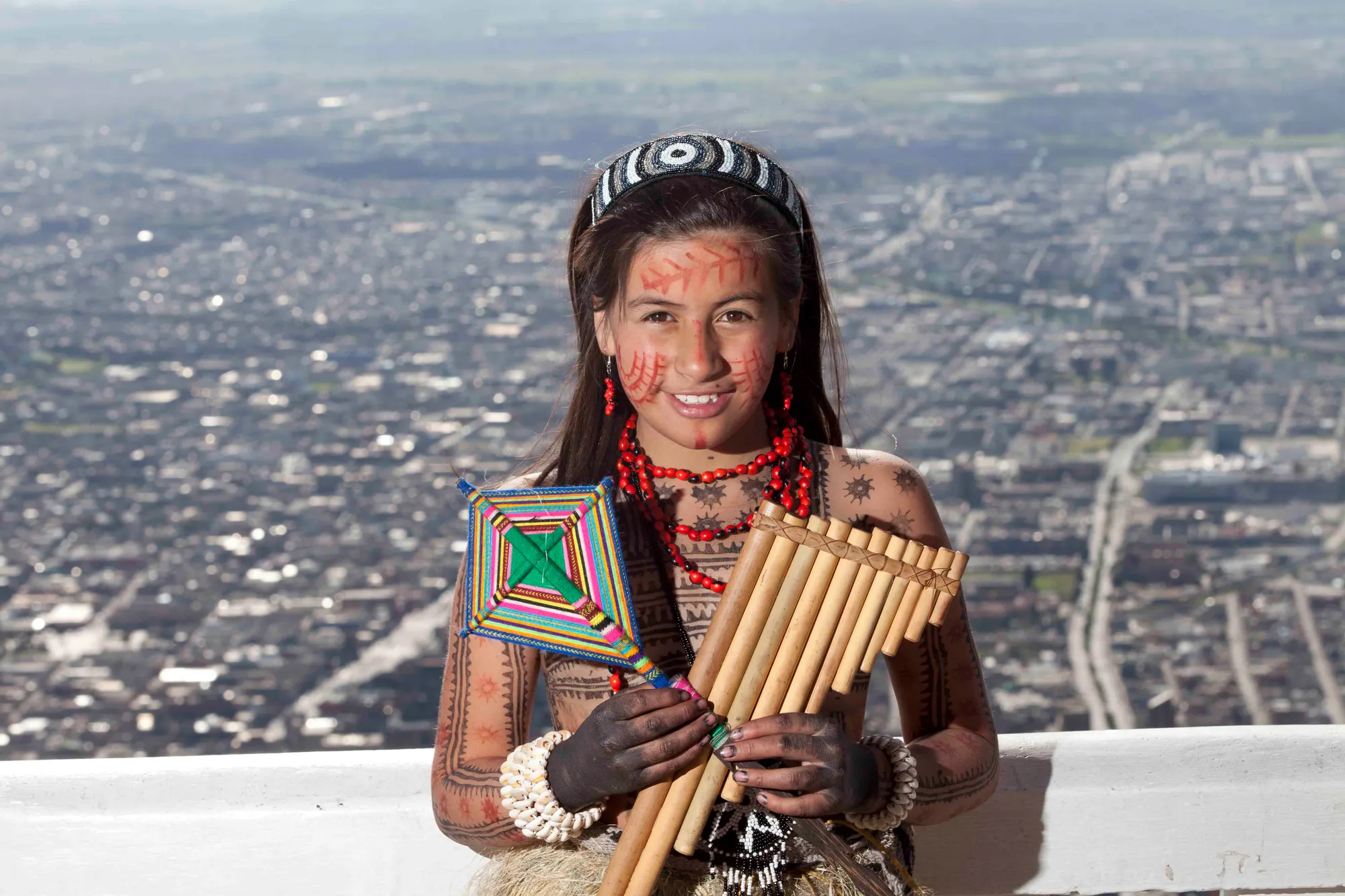Niña Tubú con flauta de pan y pintura corporal, con Bogotá al fondo